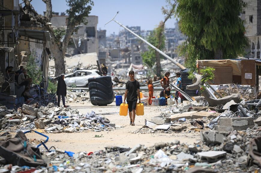 A Palestinian man carries water containers past destroyed buildings in southern Gaza's Khan Yunis