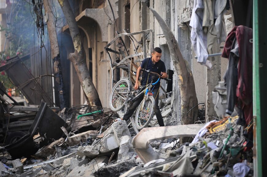 A Palestinian boy carries his bicycle as he climbs over debris a day after an operation by Israeli special forces in the Nuseirat camp in the central Gaza Strip 