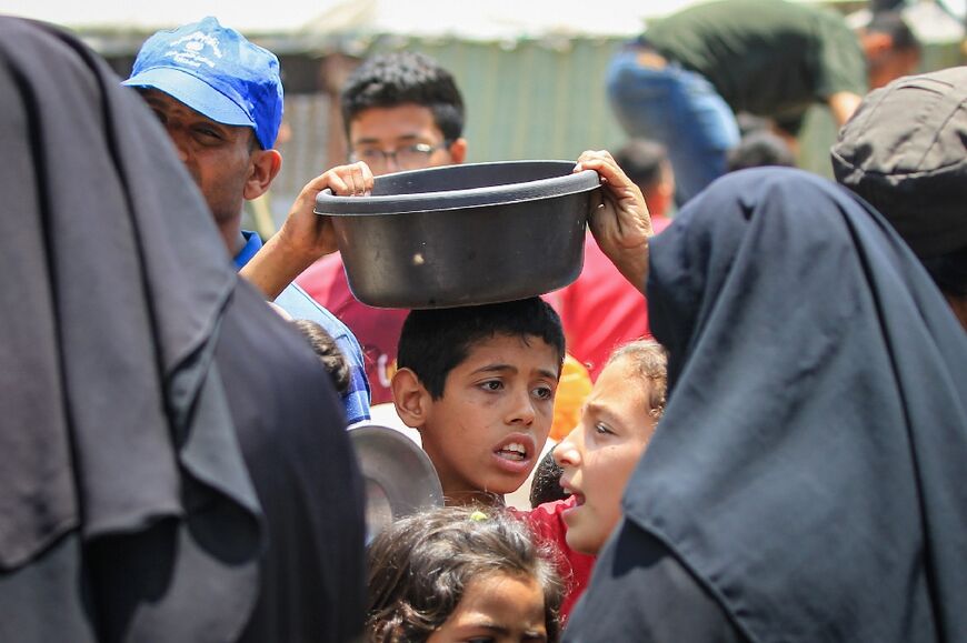 Palestinians queue for meal rations at a communal food distribution point in al-Bureij refugee camp in the besieged Gaza Strip on June 3, 2024