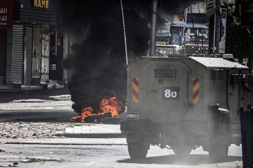 An Israeli army vehicle drives past burning tyres during a raid in the northern occupied West Bank