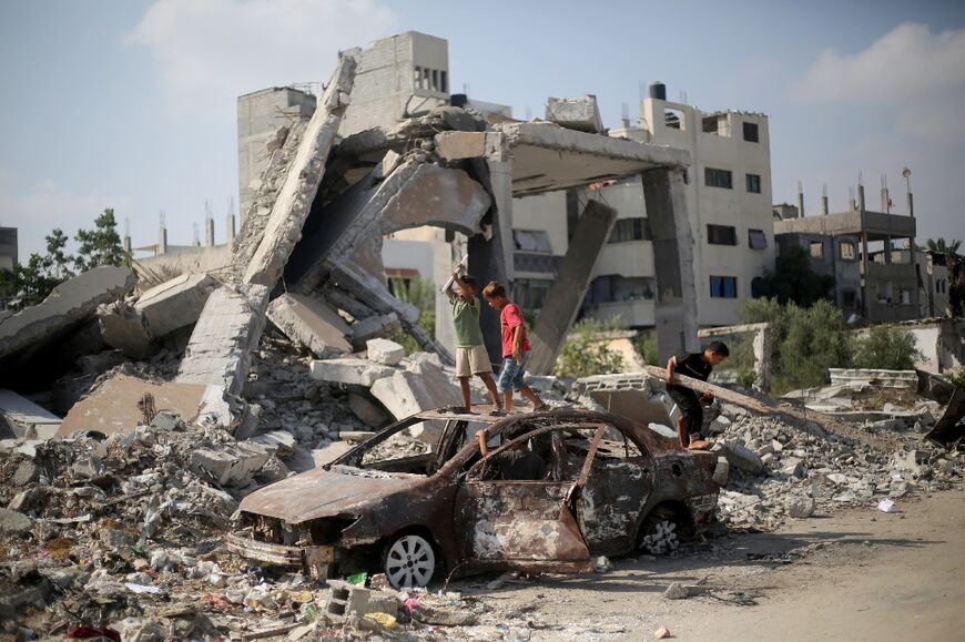 Palestinian children play on the wreckage of a car near a building destroyed in Israeli bombardment, in central Gaza's Al-Bureij refugee camp