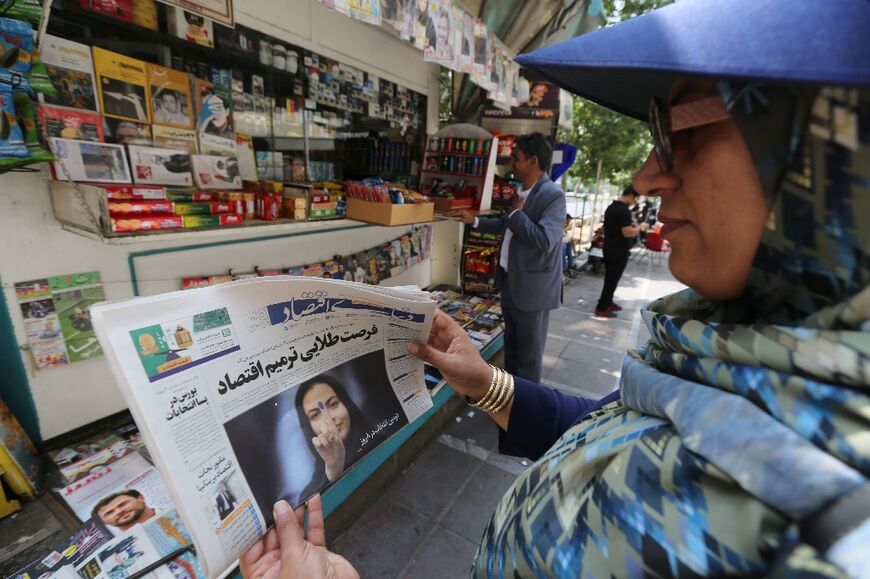 An Iranian woman looks at a newspaper headline at a stall in Tehran, the day after the runoff presidential election