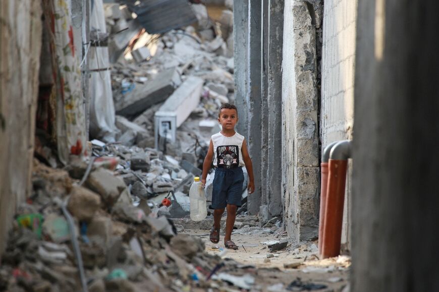 A Palestinian boy carrying an empty container as he walks in a rubble-covered alley in Khan Yunis in the southern Gaza Strip, where there are severe shortages of water and food due to the war