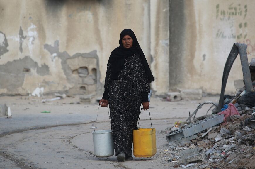 A Palestinian woman carries water containers in Khan Yunis