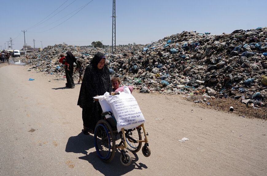 A Palestinian woman transports bags of food past a pile of garbage surrounding a camp for displaced people in Khan Yunis, southern Gaza