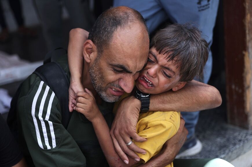A Palestinian child is comforted as he stands near a body bag at Al-Ahli Arab hospital in Gaza City