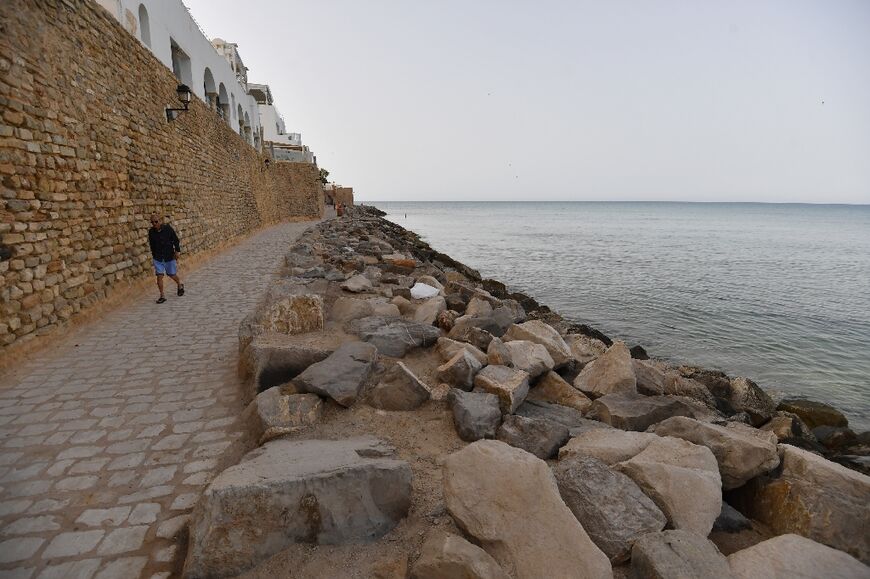 A man walks next to rock armour built to protect the coastline from erosion in the tourist town of Hammamet