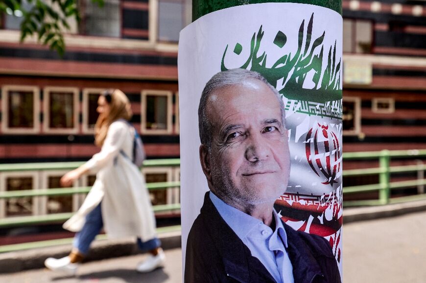A woman walks past an election poster for Iranian presidential candidate Masoud Pezeshkian