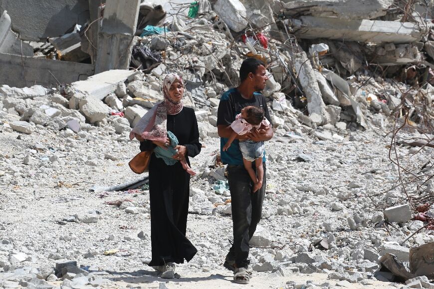 A Palestinian couple holds their children as they walk through debris in Khan Yunis in the southern Gaza Strip on July 4
