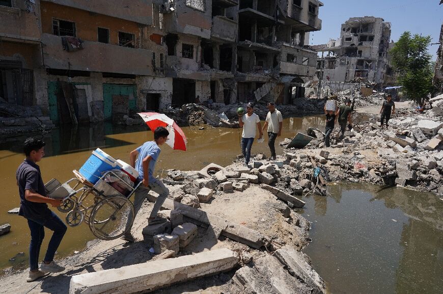 Palestinians walk on the rubble of buildings destroyed in previous Israeli bombardment, between two pools of stagnant water, in Khan Yunis