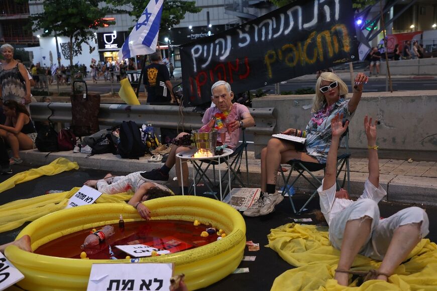 Protesters lie on the ground covered in red paint, as another wears a mask depicting Israeli Prime Minister Benjamin Netanyahu sitting near a paddling pool filled with fake blood, during an anti-government rally in Tel Aviv