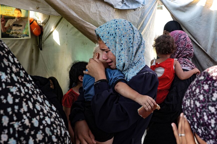 A Palestinan woman carrying a child weeps following a strike that hit tents at a central Gaza hospital courtyard