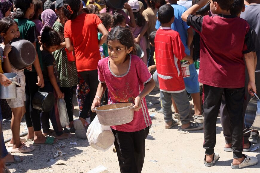 A Palestinian girl carries a pot of soup at a food distribution point in the Jabalia refugee camp