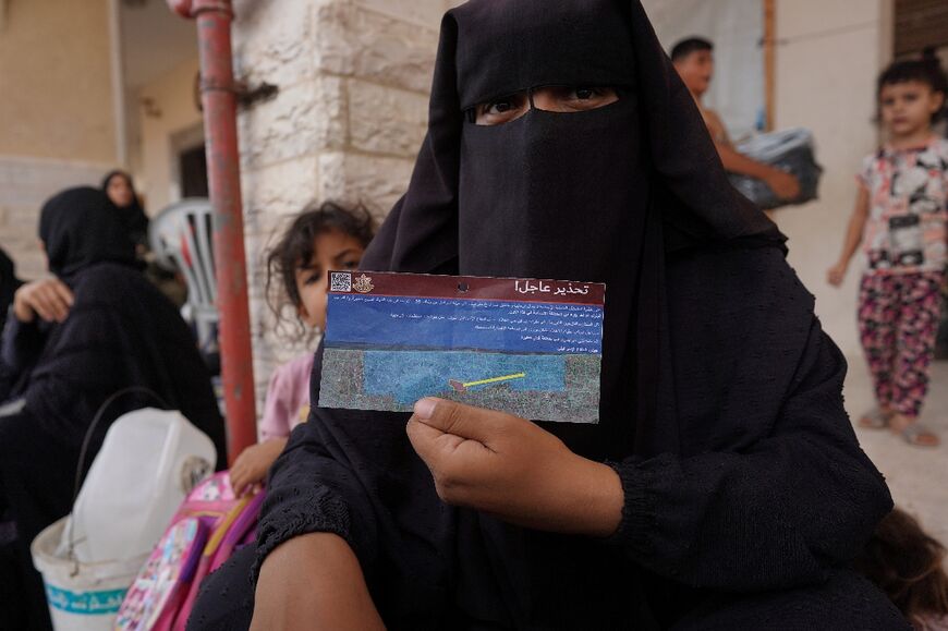 A woman shows a leaflet dropped by the Israeli military asking Palestinians to leave an area of Khan Yunis