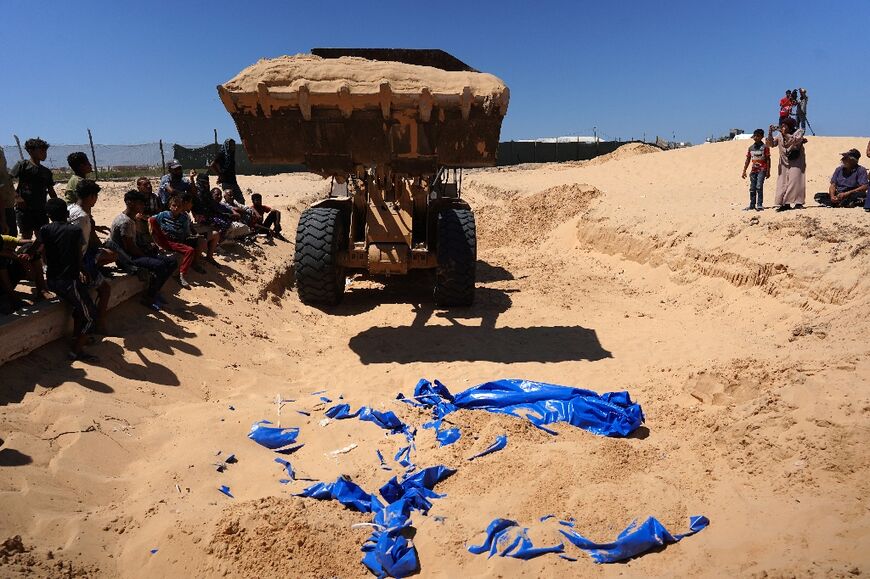 People watch as bodies that were taken and later released by Israel are buried during a mass funeral at a cemetery in Khan Yunis in the southern Gaza Strip