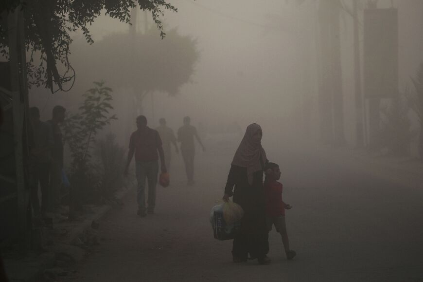 Palestinians walk through dust and smoke after Israeli troops targeted a building in the Nuseirat refugee camp in the central Gaza Strip