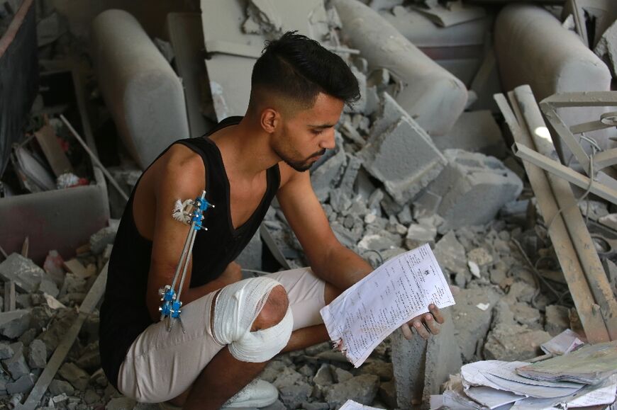 Injured Palestinian student Fares al-Farra, 19, salvages academic documents from the rubble of his home in Khan Yunis in the southern Gaza Strip