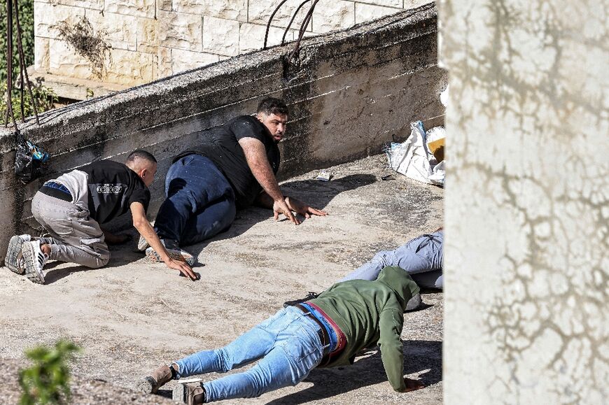 Palestinian men take cover from gunfire on the roof of a building during the raid