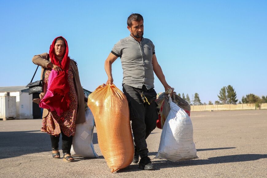 Afghan refugee Fazila Qaderi (L) and her husband carry their belongings after their deportation from Iran, at a registration centre near the Afghanistan-Iran border in the Islam Qala district of Herat province