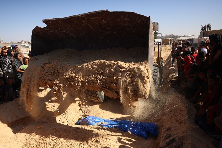 People watch as an excavator pours sand over one of the 88 bodies buried in a mass grave in Khan Yunis on September 26