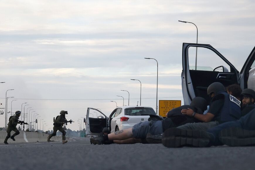 Journalists take cover behind cars as Israeli soldiers take up position during clashes with militants near Gevim kibbutz on October 7, 2023