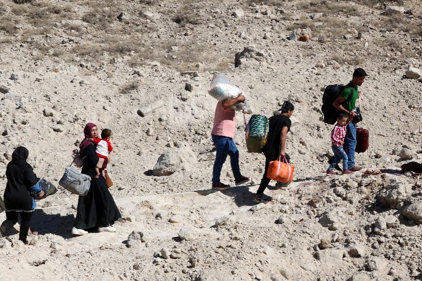 People fleeing Israeli bombardment walk around a crater caused by an Israeli strike in the Masnaa area on Lebanon's side of the border