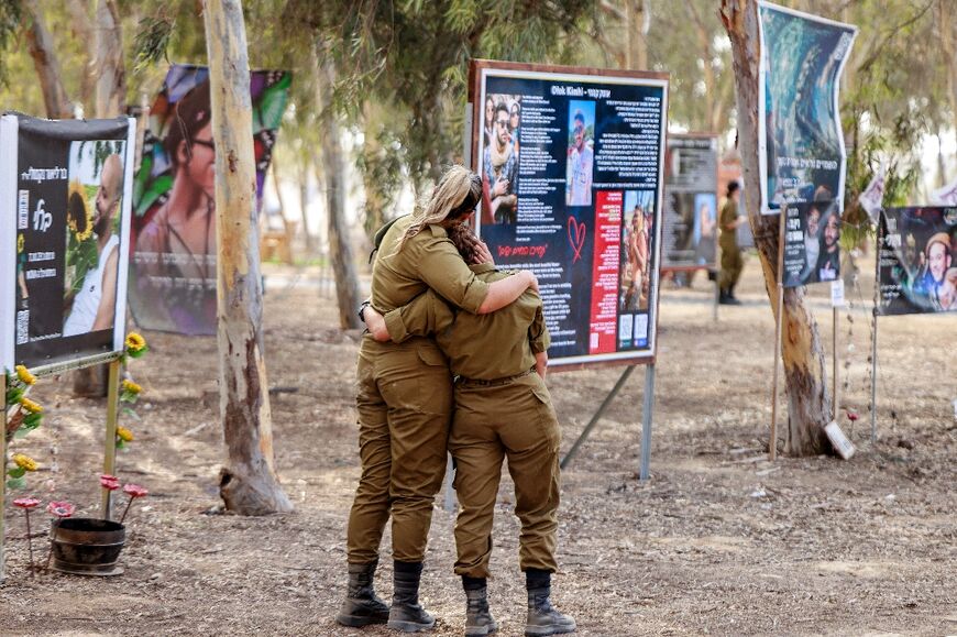 Female Israeli army soldiers embrace at a memorial for the victims killed at or kidnapped from the Nova music festival in Reim during the October 7 attacks by Palestinian militants