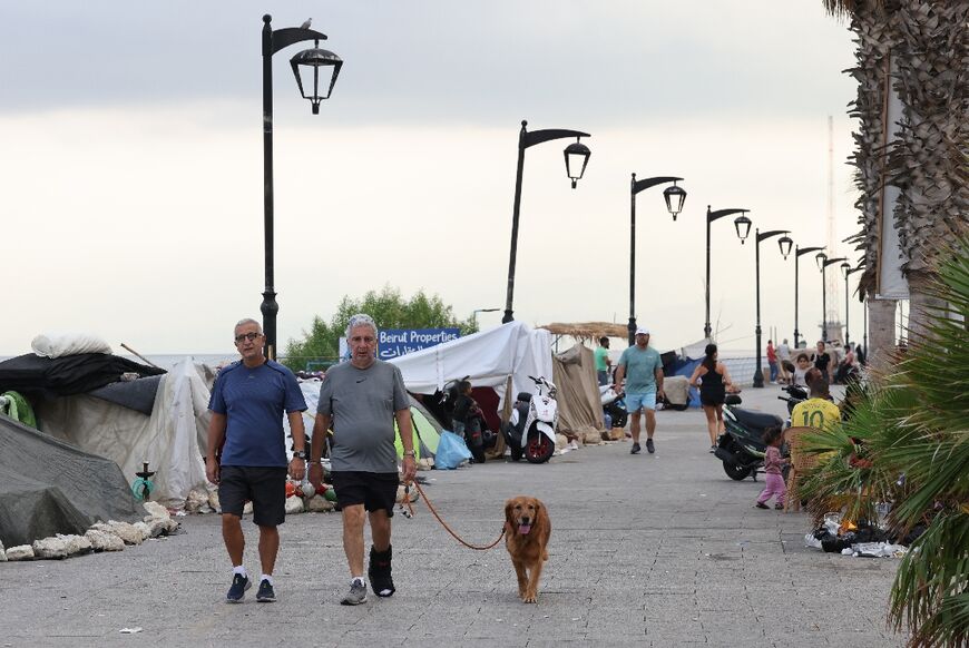 Lebanese men walk a dog past tents where displaced people have been sleeping on Beirut's seafront