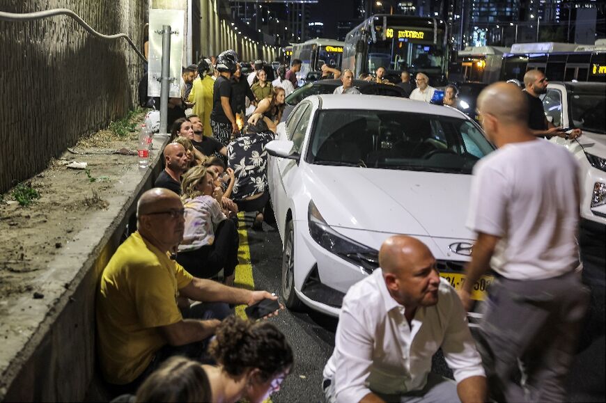 People take cover by the side of a Tel Aviv highway as sirens blare warning of incoming fire