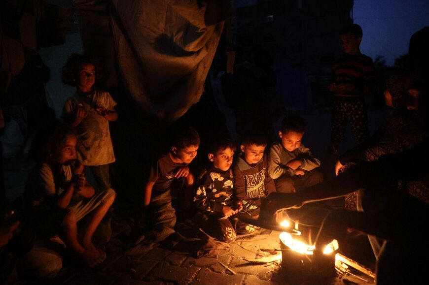 Palestinian children wait for a meal as they sit around a fire in the Bureij camp for Palestinian refugees in the central Gaza Strip