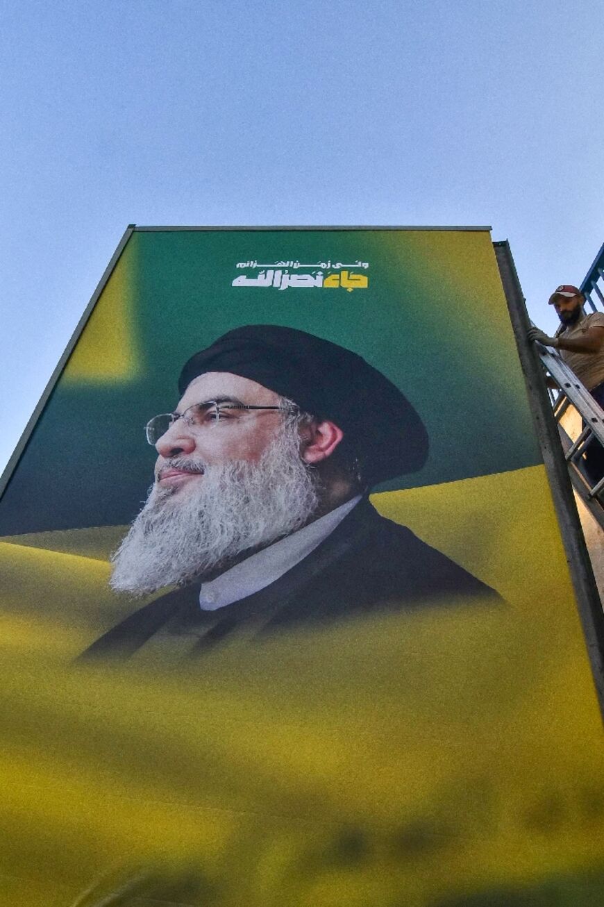 A worker puts up a portrait of slain Hezbollah leader Hassan Nasrallah on a roadside billboard on the main highway to Beirut airport