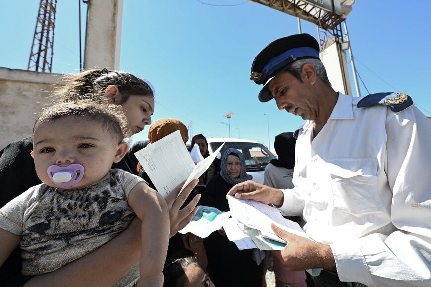 A border policeman checks the documents of a woman carrying an infant as she enters Syria from Lebanon