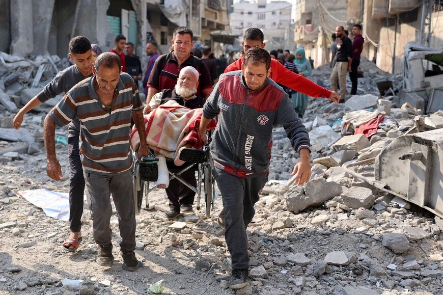 Five Palestinians help an elderly man in a wheelchair to make his way past the shattered house