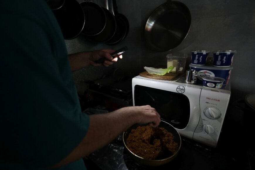 A man prepares an order using his smartphone light in the kitchen of a cafe in Tehran during electricity outage