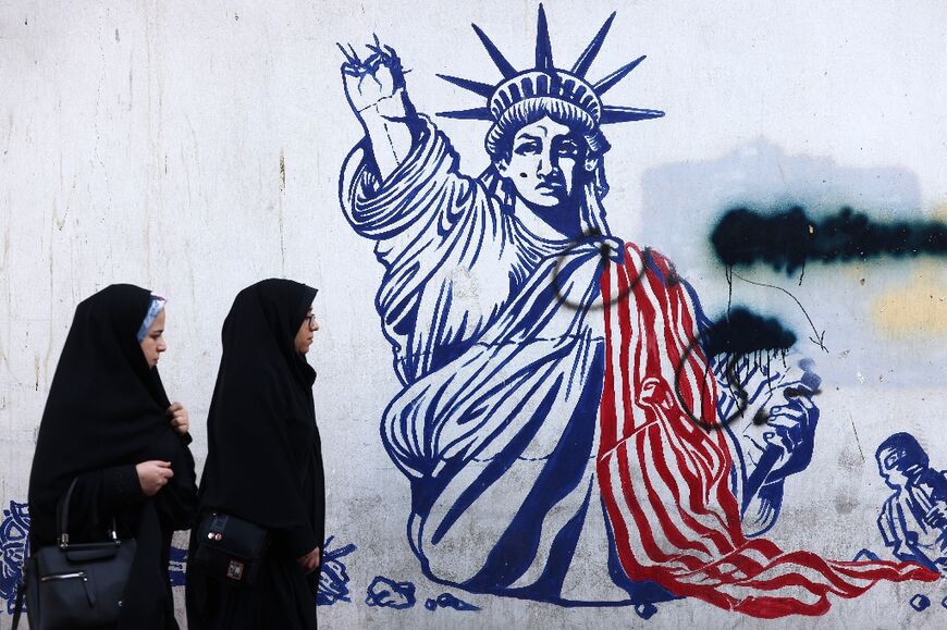 Women walk past a mural of the Statue of Liberty, her torch-bearing arm broken, painted on the wall of the former US embassy in Tehran