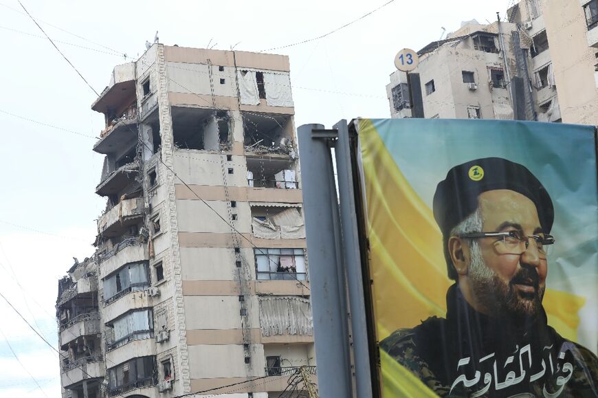 A portrait of Hezbollah's slain commander Fuad Shukr hangs in front of buildings damaged in recent Israeli strikes