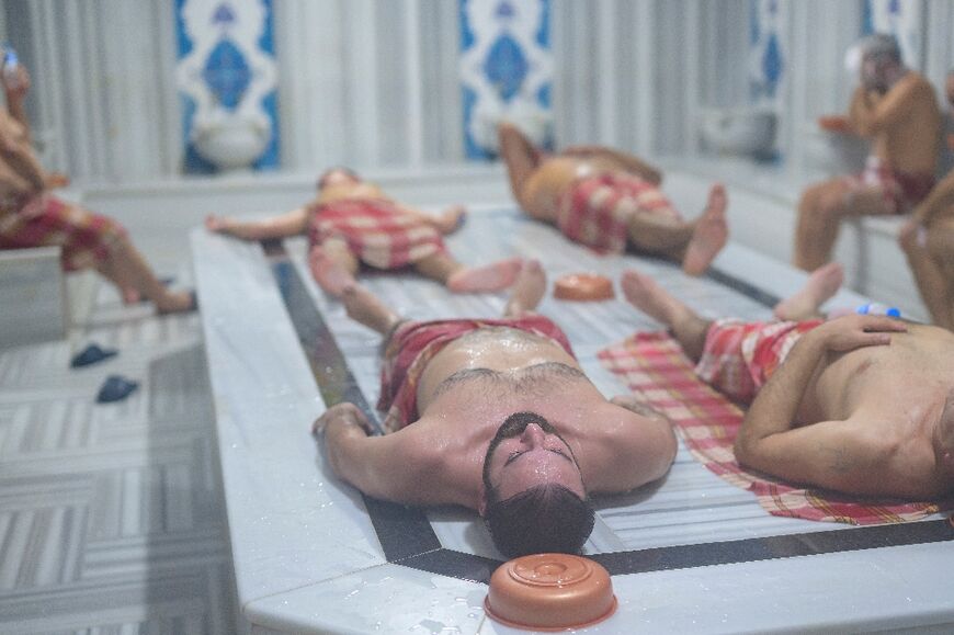 Lying on a heated marble slab, people relax inside a modern hammam, enjoying the centuries-old tradition of ritual bathing