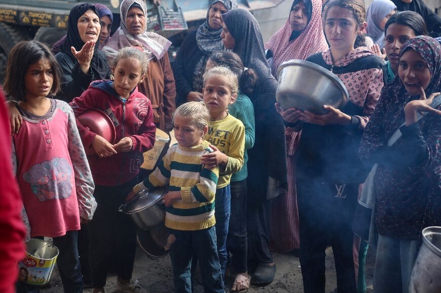 Displaced Palestinians gather to receive a hot meal at a central Gaza refugee camp