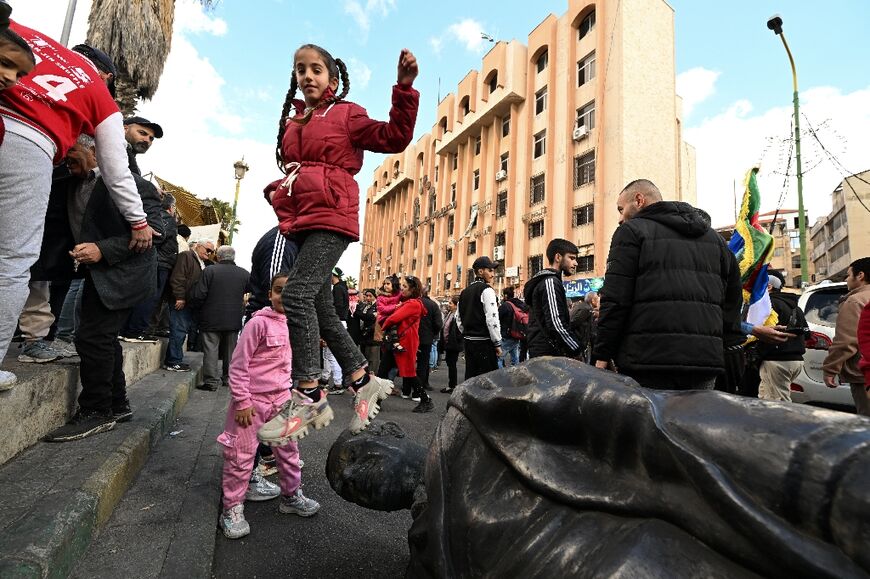 A girl jumps off a toppled statue of Syrian ex-president Hafez al-Assad during celebrations in the city of Sweida