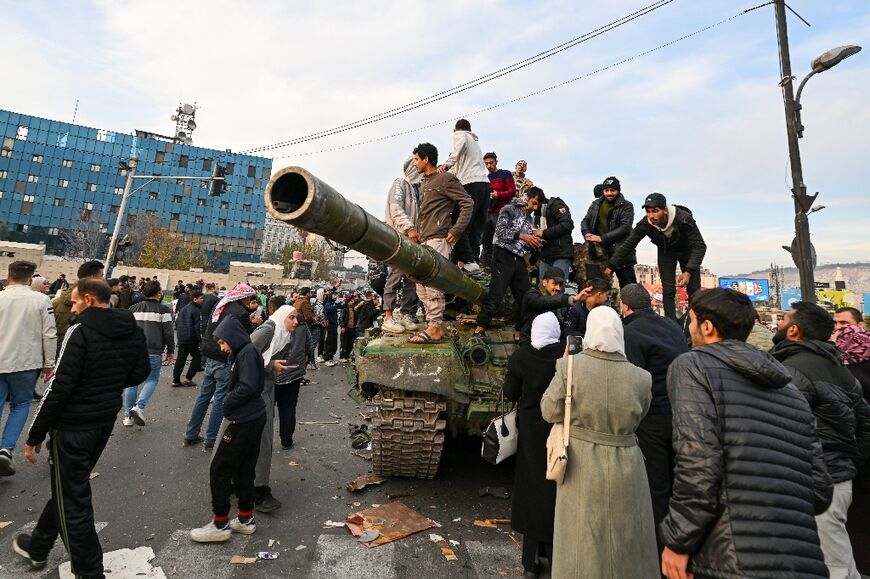 People stand atop a tank celebrating at Umayyad Square in Damascus