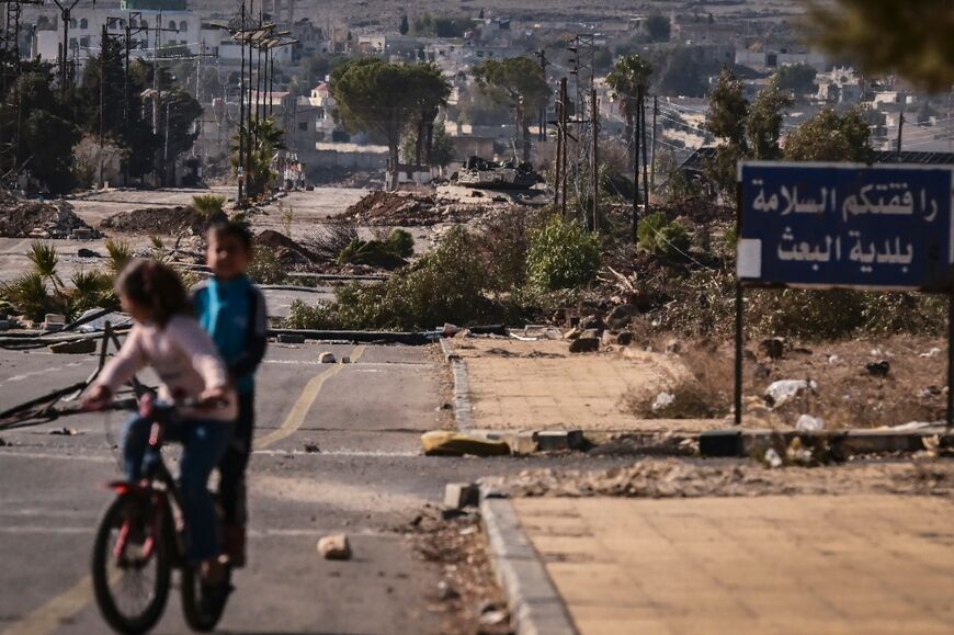 Syrian children ride their bicycles around the debris left by the passage of an Israeli tank through Baath City