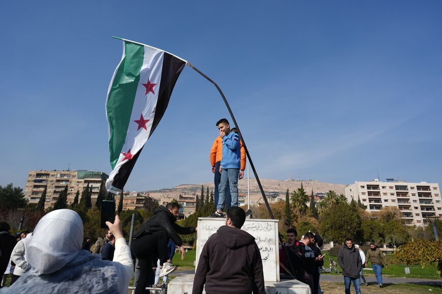 In Damascus, a young boy stands beneath Syria's new flag, which was adopted by activists and rebels during the country's 2011 revolution. Photo taken on December 11, 2024. Photo credit: Morhaf Kiwan.