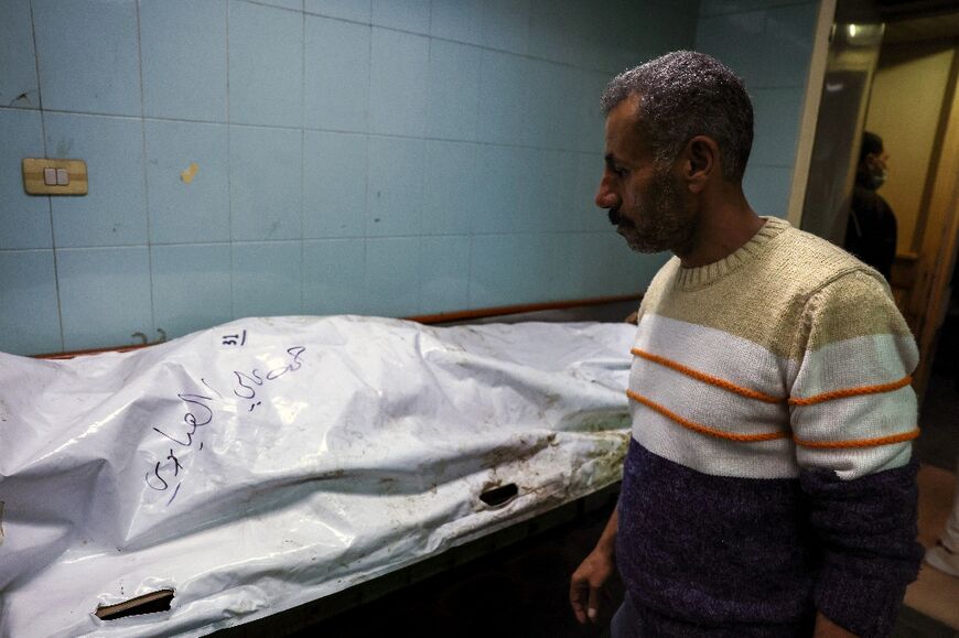 A man searches for relatives among bodies that show signs of torture beneath their white shrouds.