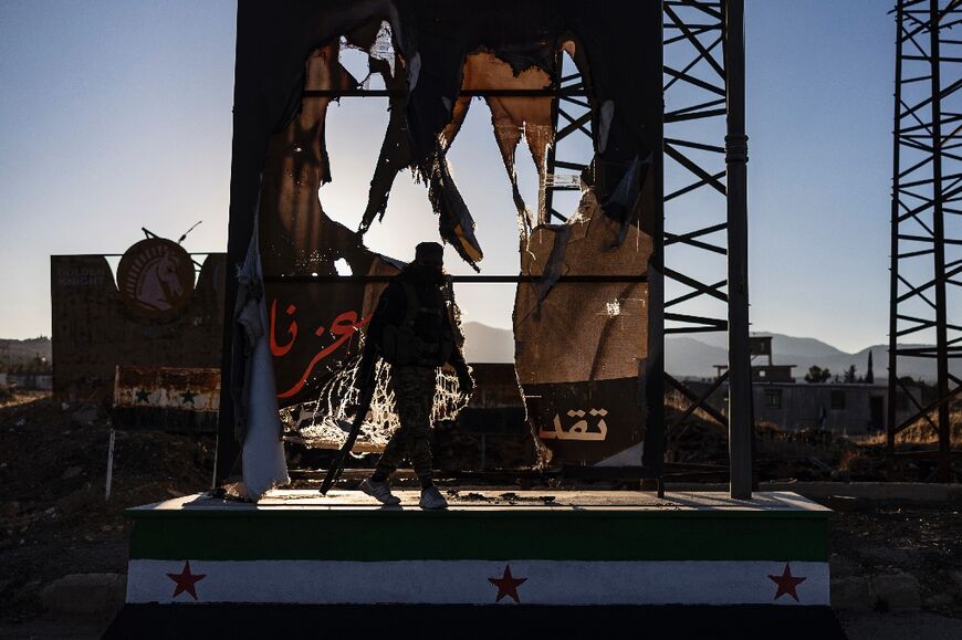 A rebel fighters walks past a defaced portrait of the toppled Syrian president Bashar al-Assad, in the town of Yafour near Damascus