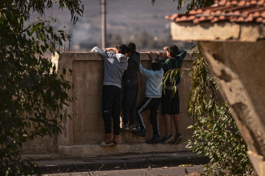 Syrian children peek over a wall at an Israeli army checkpoint in Baath City