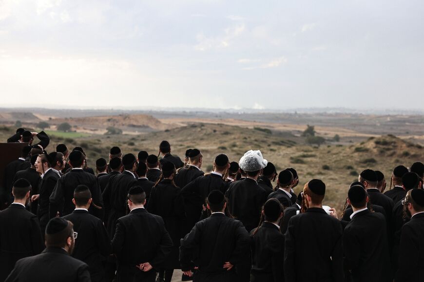 Israeli ultra-Orthodox Jewish men gather on a hill in the southern city of Sderot, watching Israeli forces bombard the northern Gaza Strip